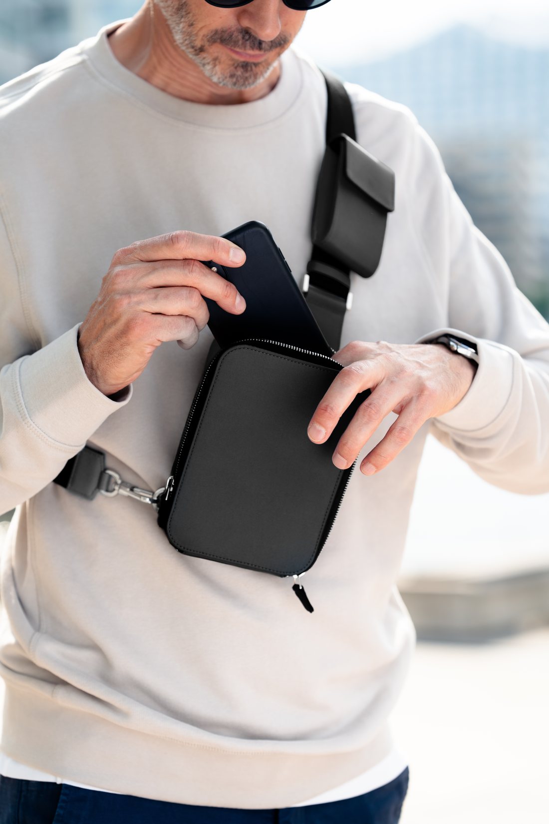A hand placing a phone into the zippered main compartment of The Verso.